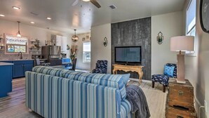A modern living room with a large sofa, a television, and a dining area with a kitchen in the background. - East Bay Vacation Rental w/ Dock! (Gulf Breeze)