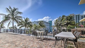 Een terras met een metselstenen vloer, buitenmeubilair, palmbomen en een uitzicht op een hotelgebouw.