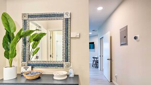 Un baño con un espejo grande, un lavamanos, una planta en maceta y un borde decorativo de azulejos.
