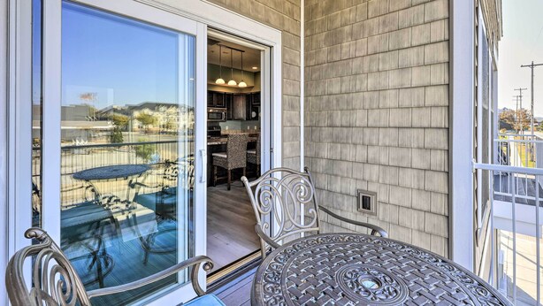 A balcony with a glass door leading to a kitchen area, a metal chair, and a table. - Dtwn Ludington Condo: Balcony, Walk To Beach! (Ludington)