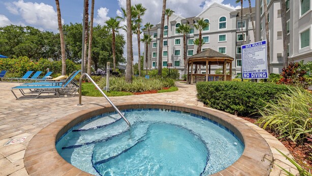A swimming pool with a hot tub, surrounded by palm trees and lounge chairs, with a spa rules sign visible. - Orlando Family Condo ~ 9 Mi to Magic Kingdom! (Orlando)