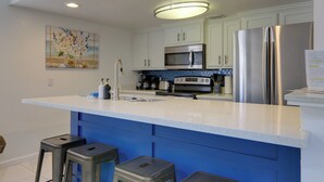 A modern kitchen with white cabinets, a stainless steel refrigerator, a microwave, and a coffee maker. - Beach Digs: Walk to Restaurants, Bars & Ocean (South Padre Island)