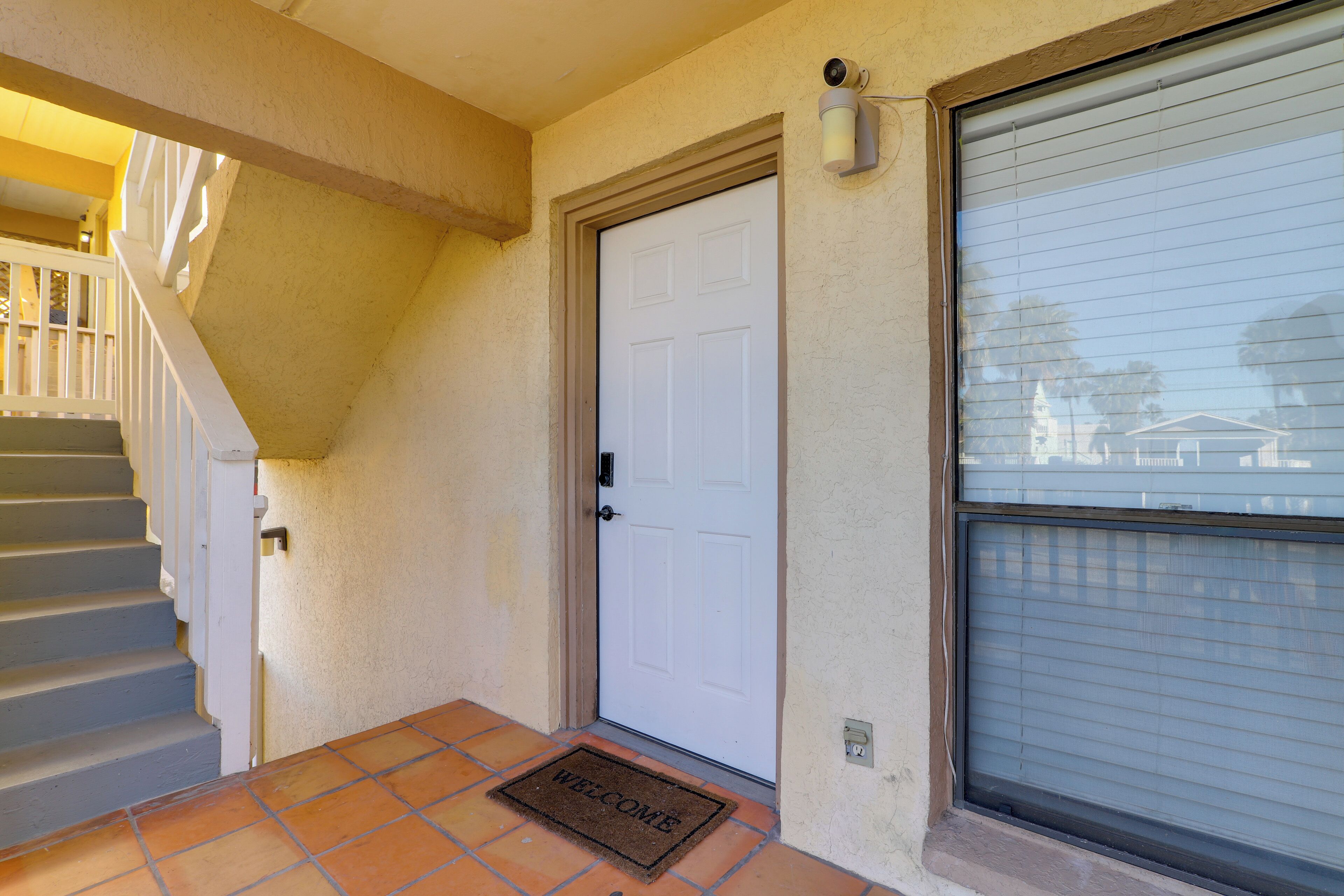 A residential entrance with a white door, a welcome mat, a staircase, and a garage door.