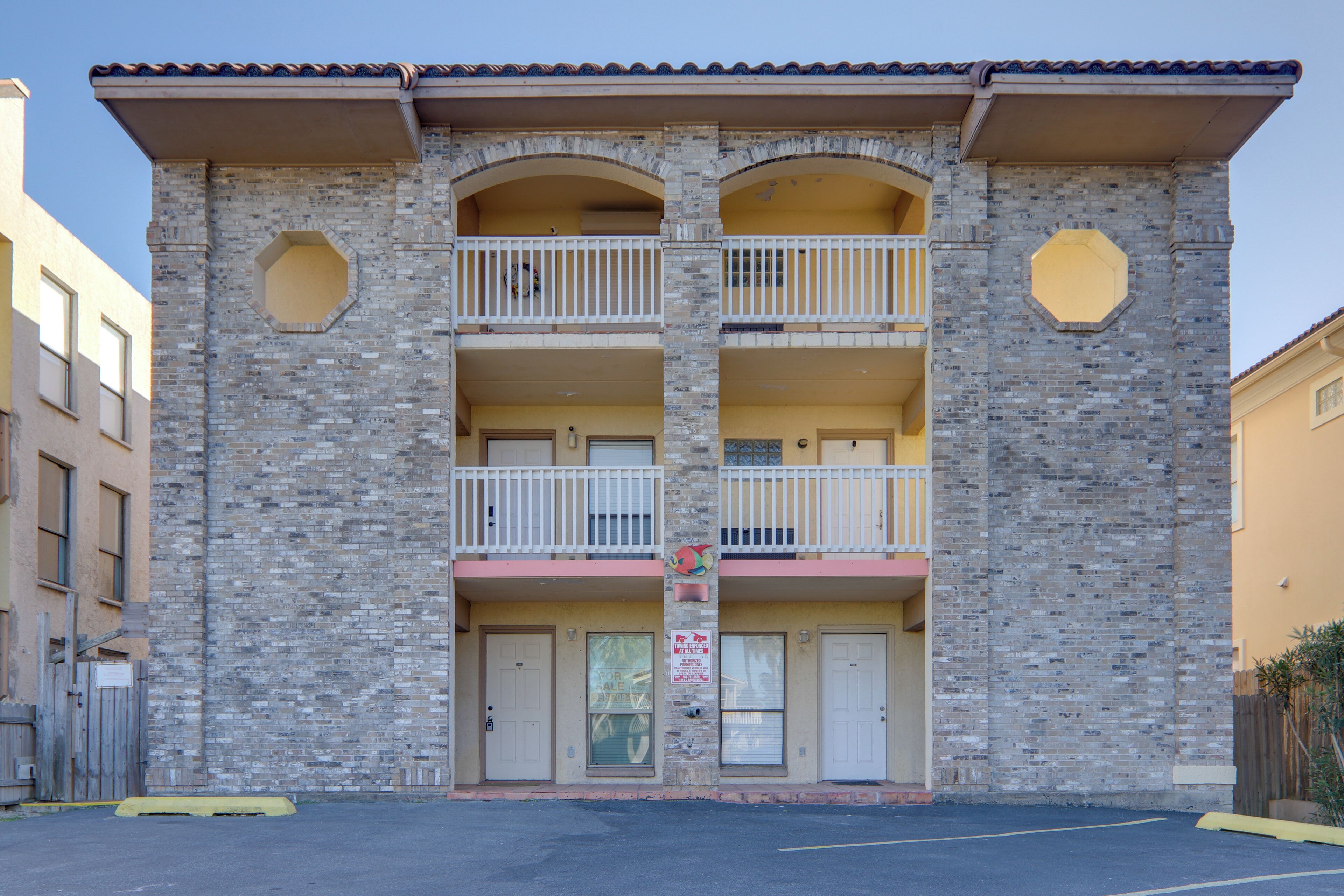 A two-story building with a brick facade, two balconies on each floor, and a flat roof.