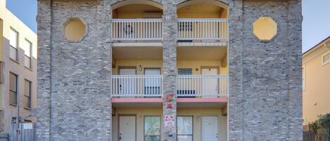 A two-story building with a brick facade, two balconies on each floor, and a flat roof.