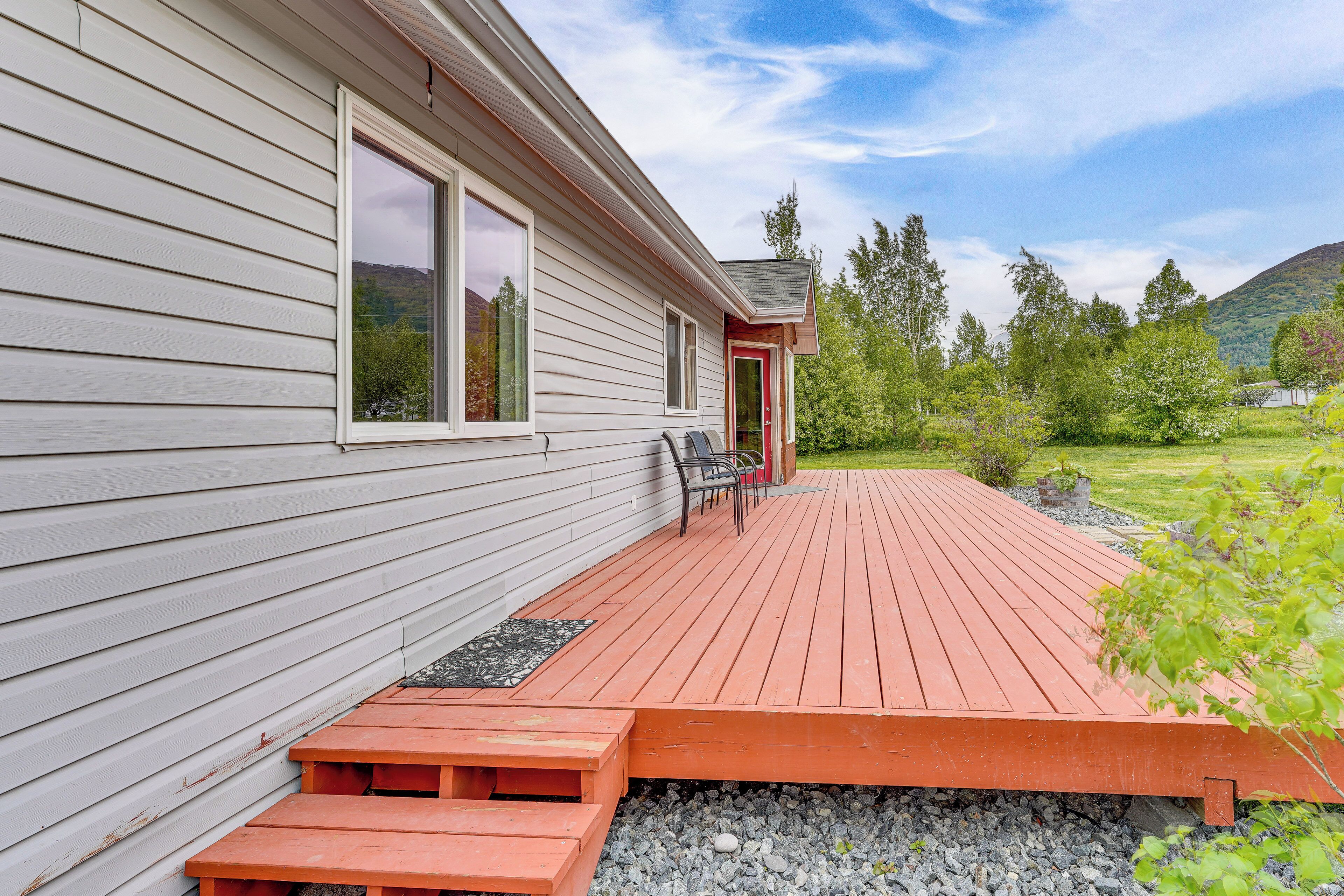 Une maison avec une terrasse en bois, une porte rouge et une vue sur un paysage verdoyant.