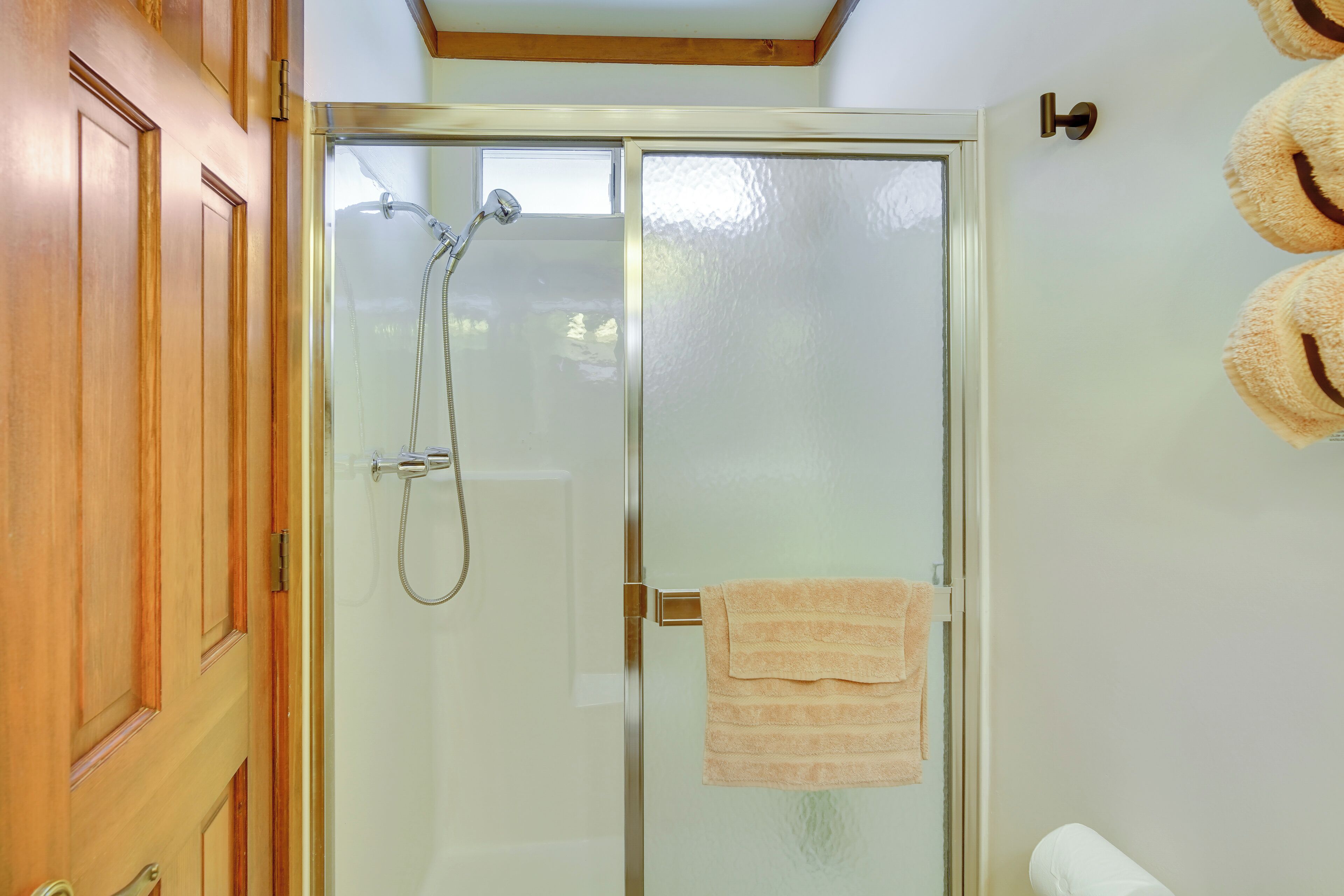 A glass-enclosed shower with a towel hanging on the door, wooden doors, and a towel rack with fluffy towels.