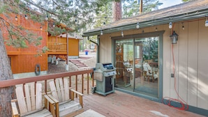 Una terraza de madera con mobiliario exterior, una parrilla y una puerta de vidrio que da a un porche cubierto.