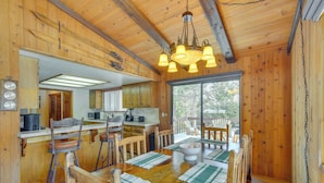 Interior de una cabaña de madera con comedor, cocina y ventanas amplias.