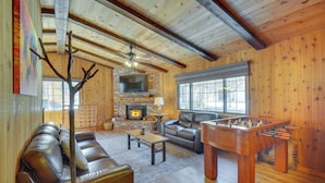 Una sala de estar acogedora con chimenea, sofá de cuero y una mesa de futbolín.
