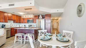 A modern kitchen with wooden cabinets, stainless steel appliances, and a dining area with white chairs and a round table set for four.