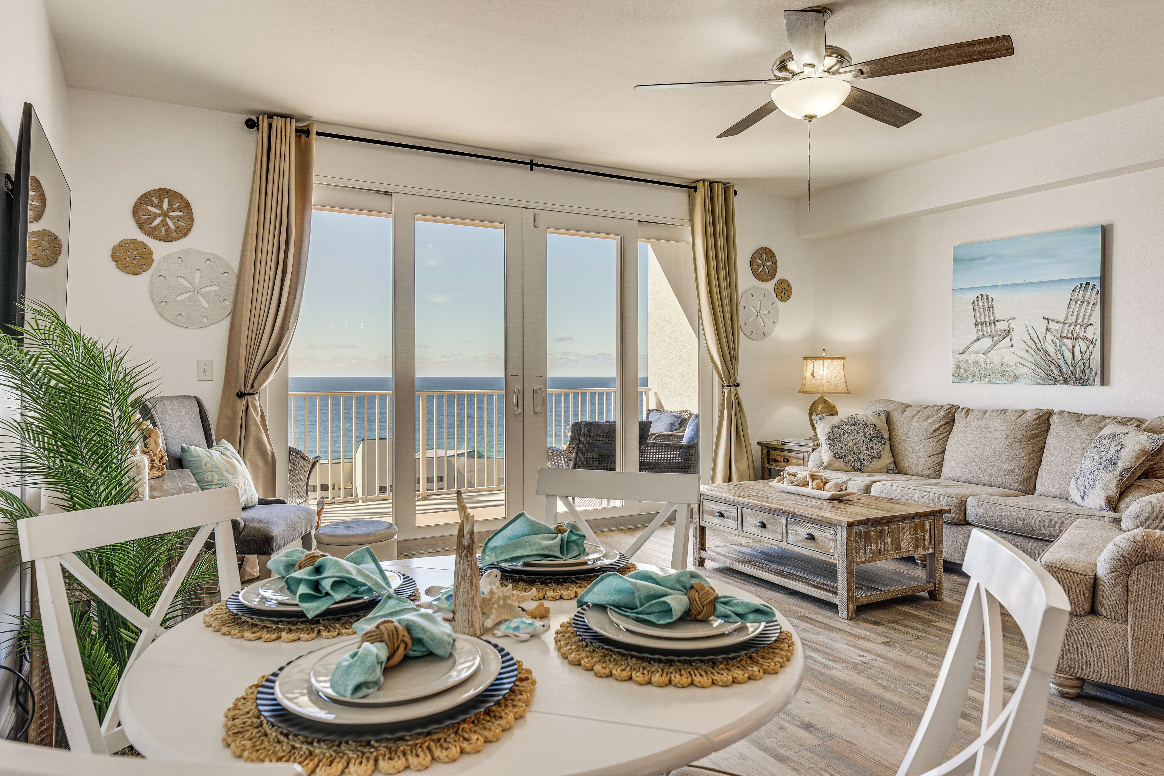 A dining area with a table set for four, a ceiling fan, and a view of the ocean through large sliding doors.