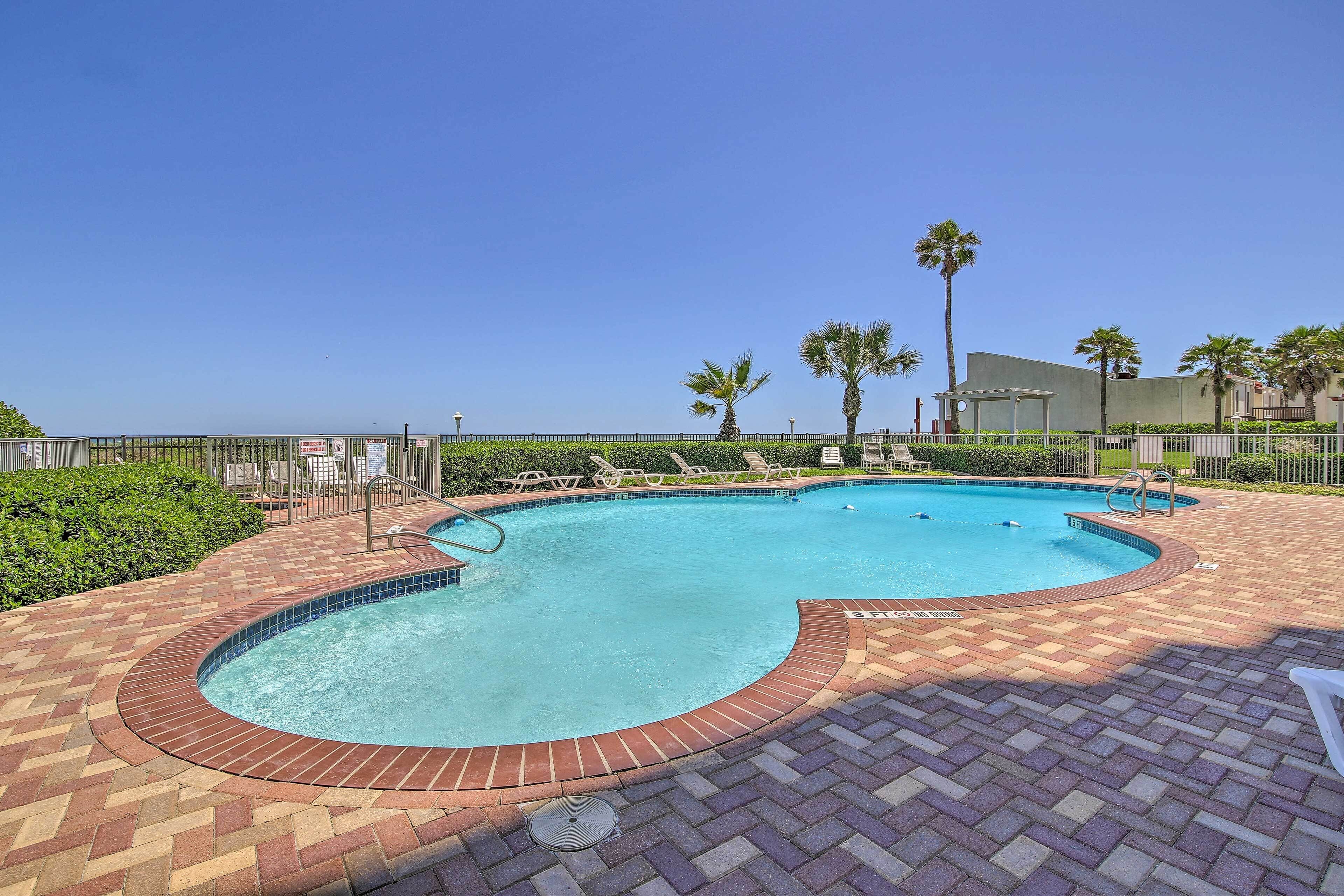 A swimming pool with a curved edge, surrounded by a brick patio and palm trees.