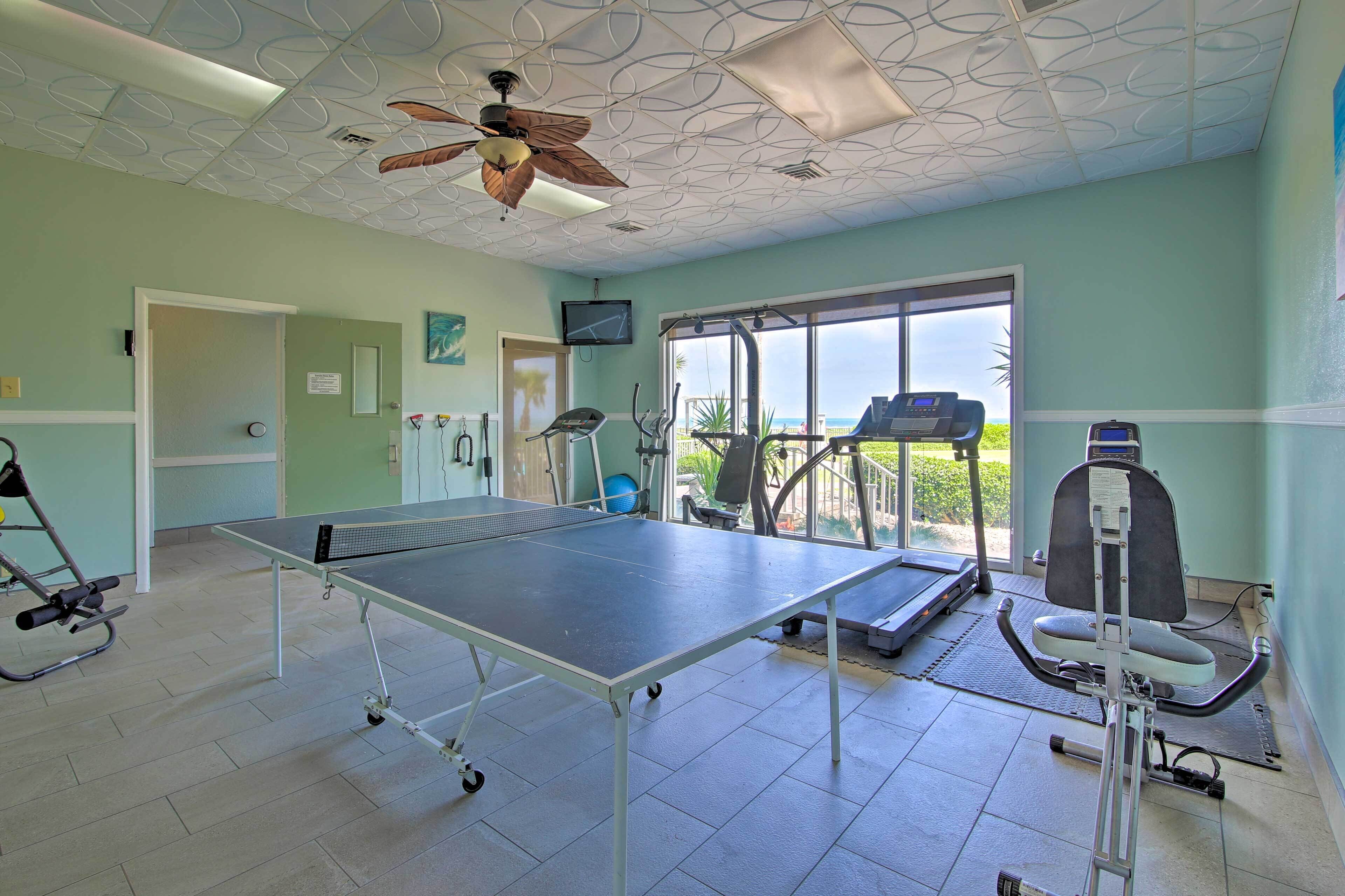 A fitness room with exercise equipment, a ping pong table, and a ceiling fan.