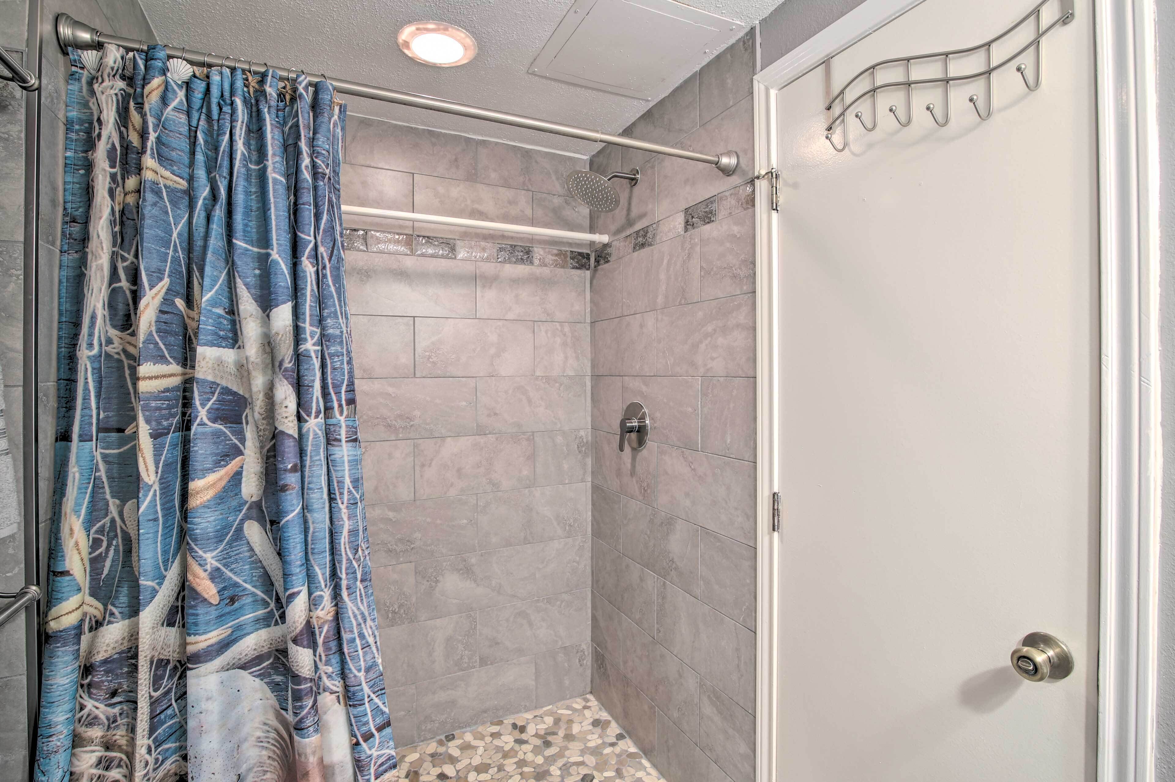 A shower with a curtain, tiled walls, a metal showerhead, and a door with a handle.