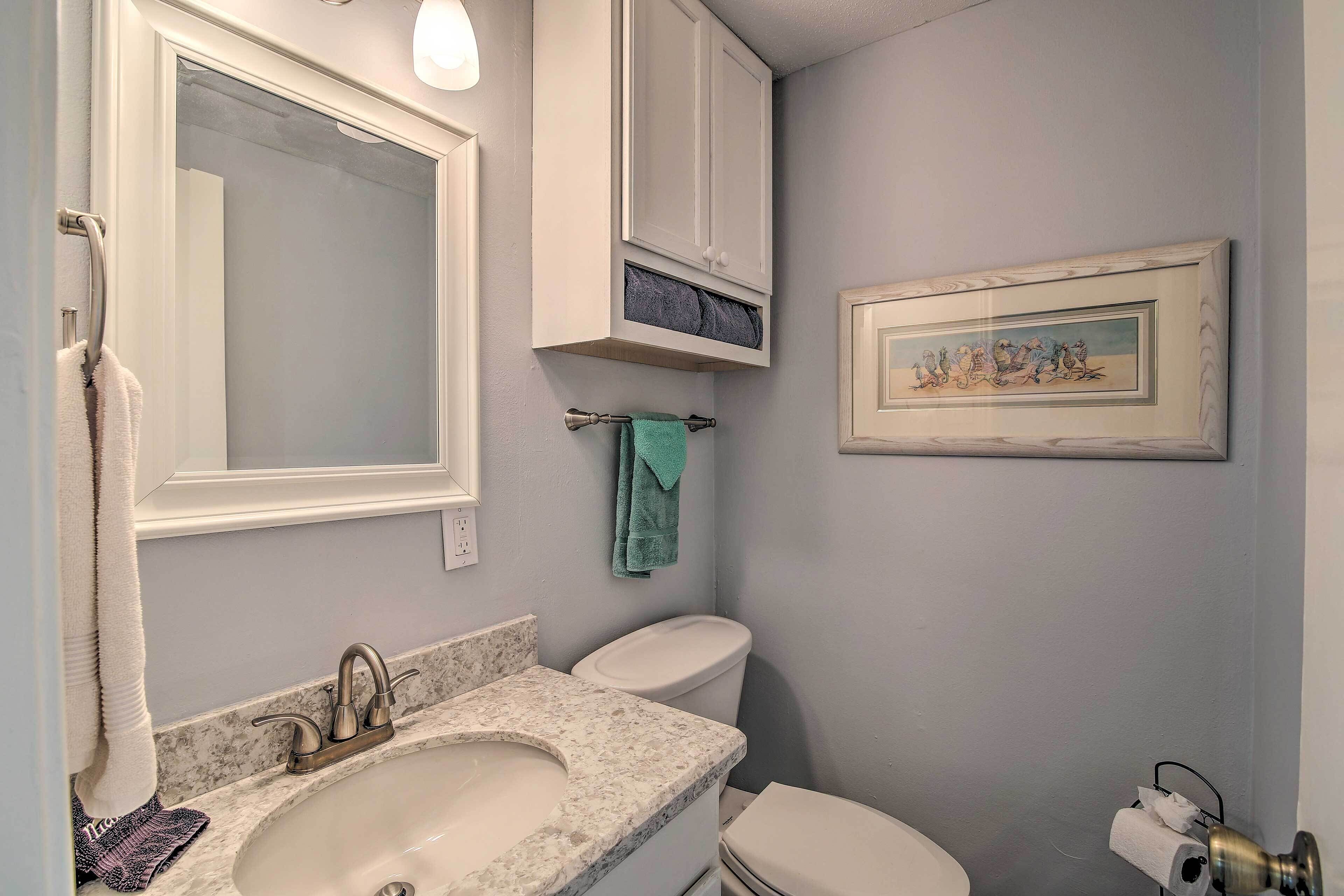 A bathroom with a sink, mirror, toilet, and framed artwork on the wall.
