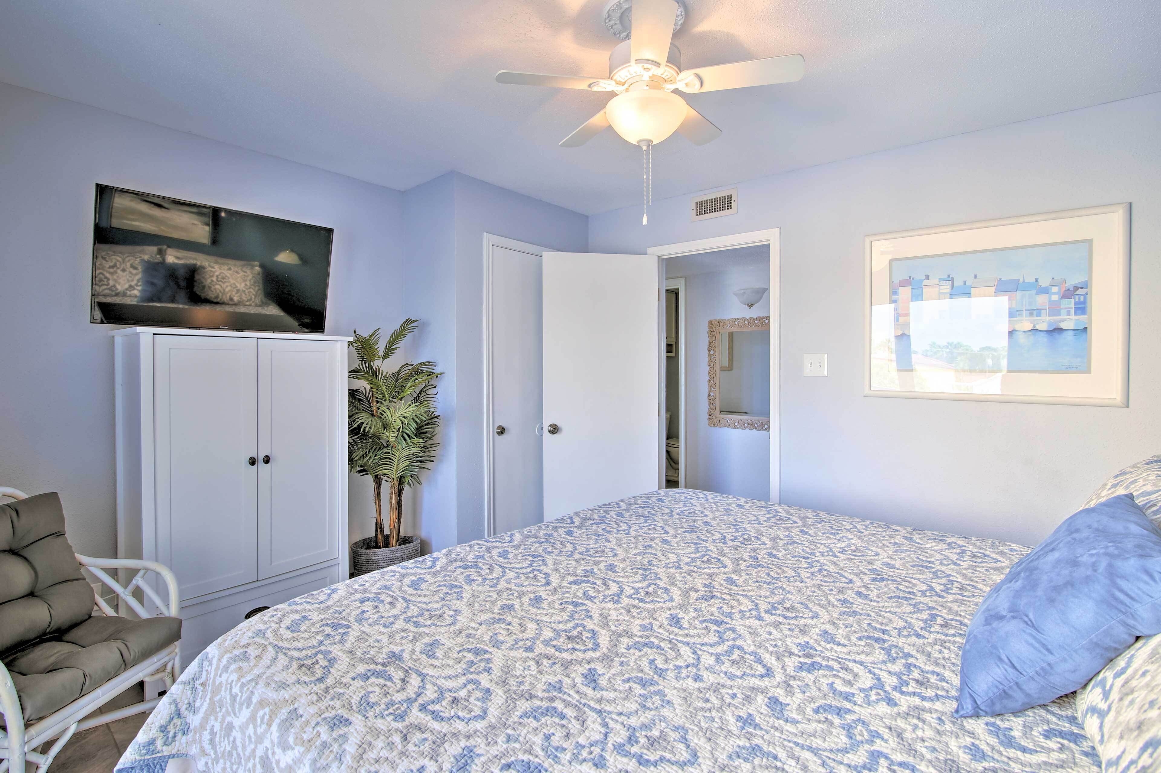 A bedroom with a bed, a ceiling fan, a wardrobe, a chair, and a potted plant.