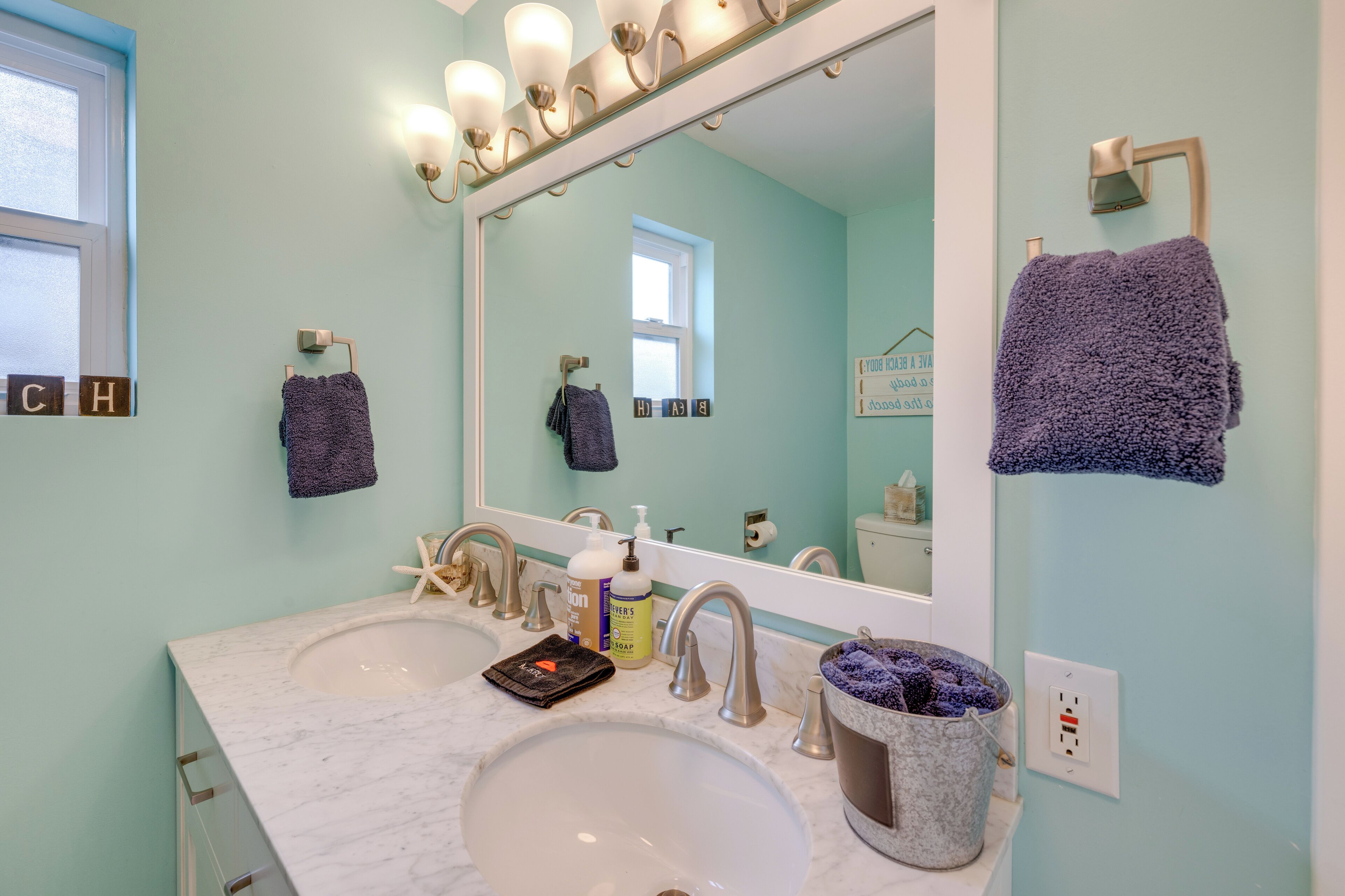 Une salle de bain avec deux lavabos, un grand miroir et une décoration en forme d’étoile de mer.