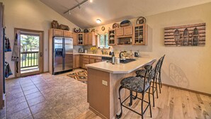 A kitchen with wooden cabinets, a stainless steel refrigerator, a large island with bar stools, and a view of the outdoors through a sliding glass door. - Pagosa Springs Home w/ Deck & Grill, Walk to Town! (Pagosa Springs)