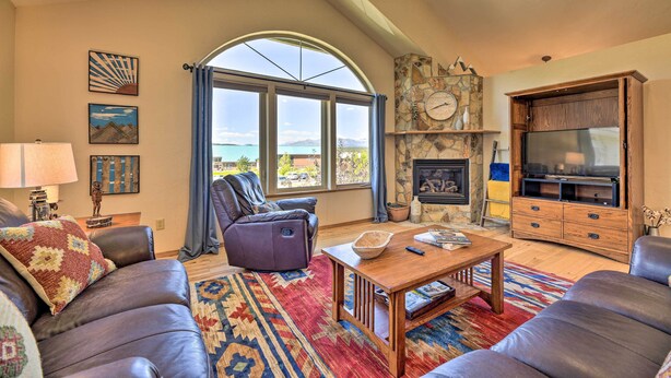 A living room with leather sofas, a wooden coffee table, a stone fireplace, and a large arched window overlooking a scenic view. - Pagosa Springs Home w/ Deck & Grill, Walk to Town! (Pagosa Springs)