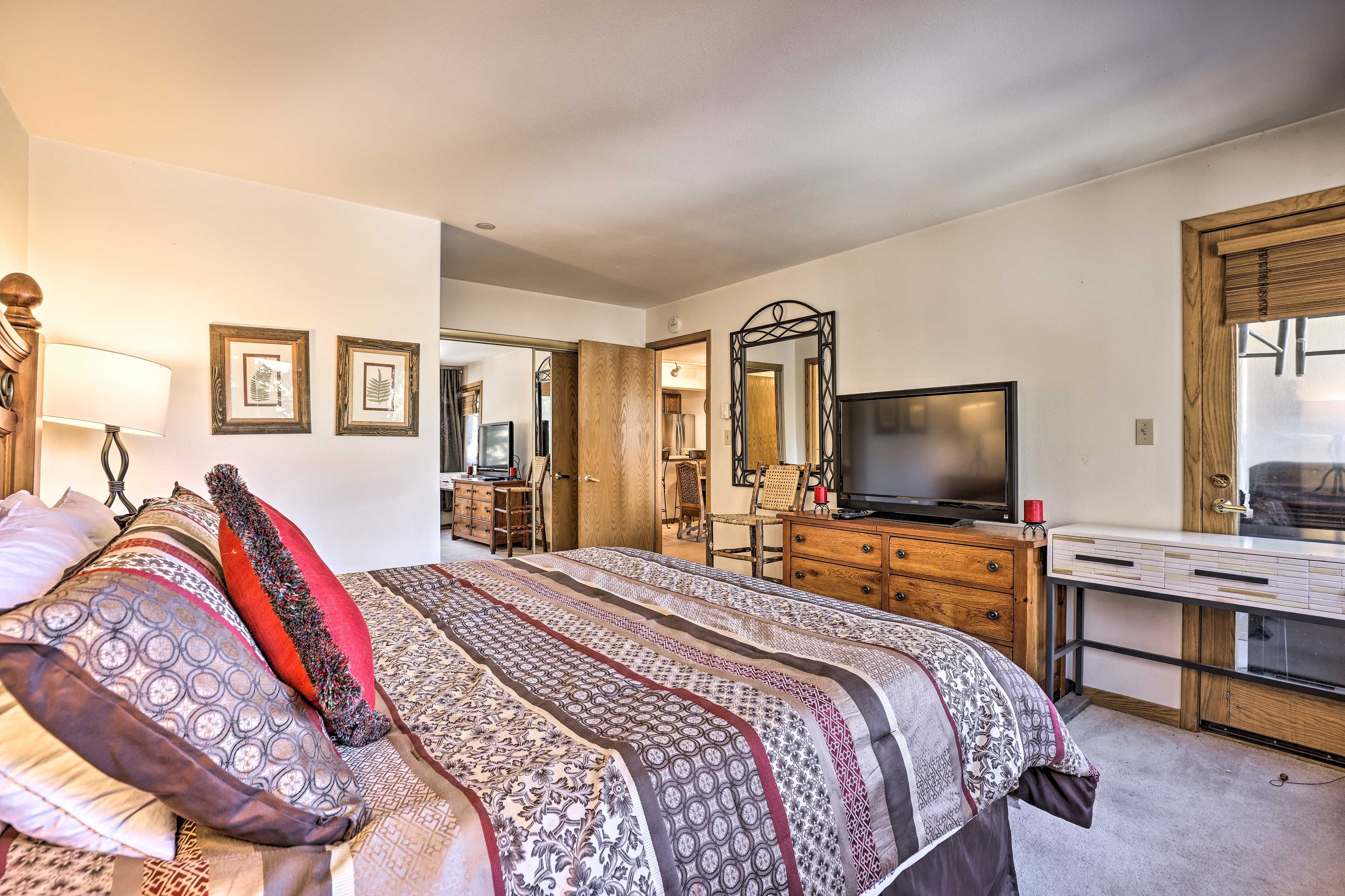 A bedroom with a large bed, a desk, a television, and a mirror.