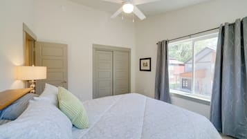 Quarto com cama, ventoinha no teto, janela com cortinas e porta.