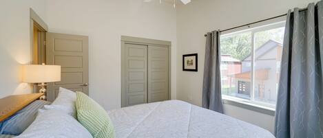 Un dormitorio con cama, ventilador de techo, ventana con cortinas y una puerta.
