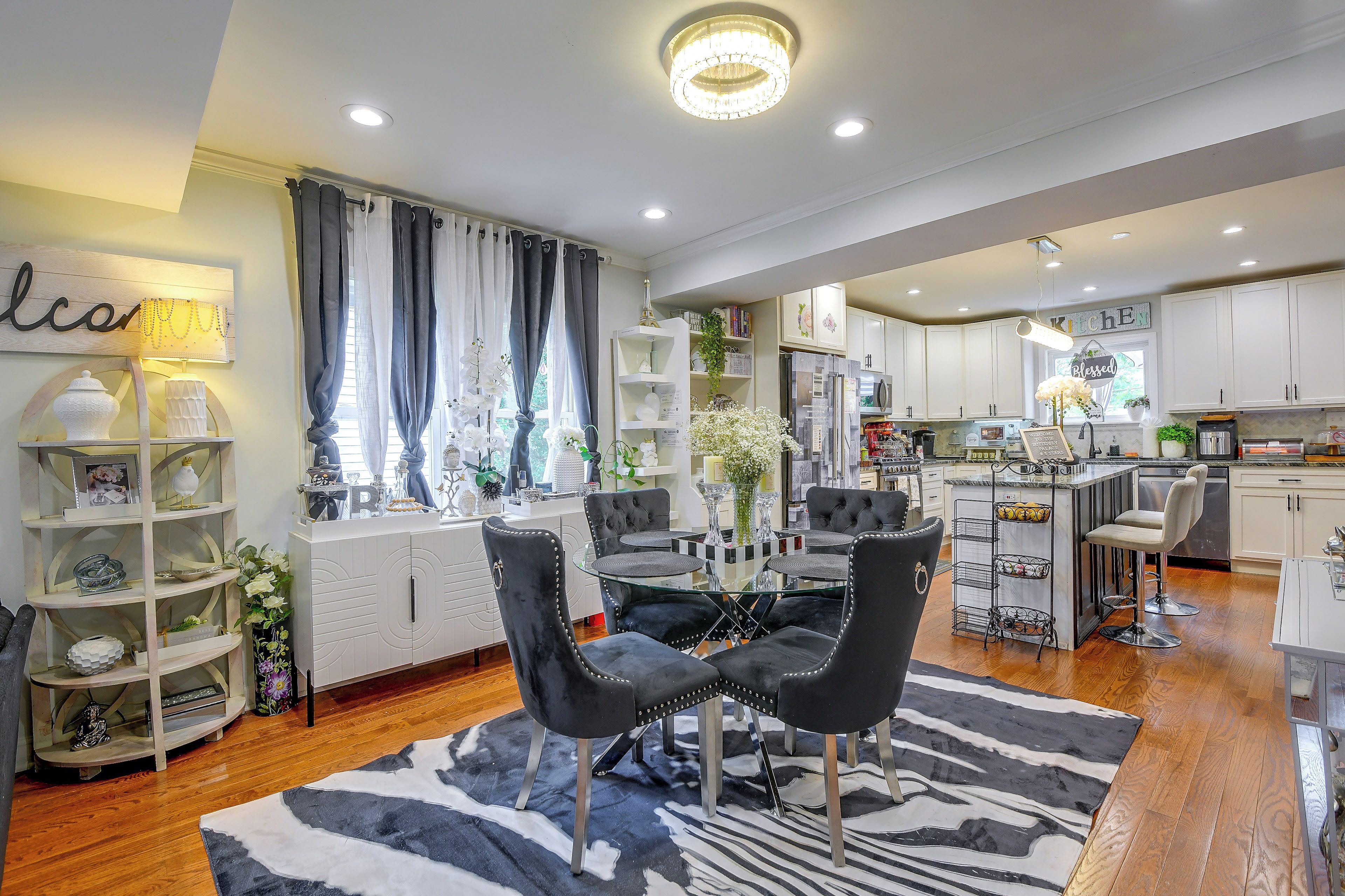 A modern kitchen with white cabinets, a central island, and a dining area with black chairs and a zebra-patterned rug.
