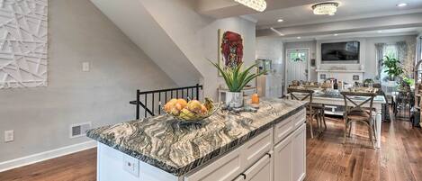 A modern kitchen with a granite countertop, a dining area with wooden chairs, and a staircase.