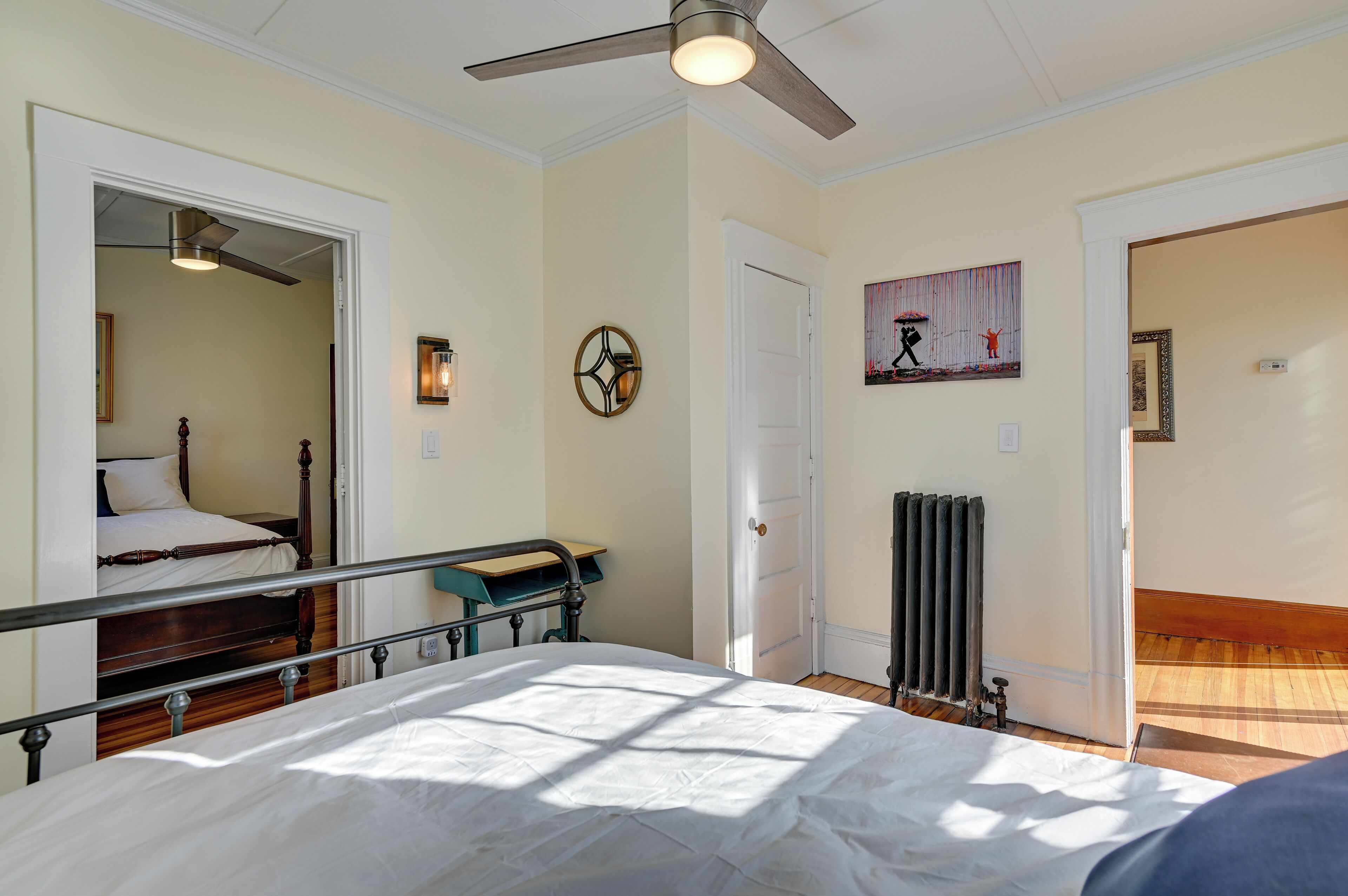 A bedroom with a bed, a ceiling fan, a radiator, and a door leading to another room.