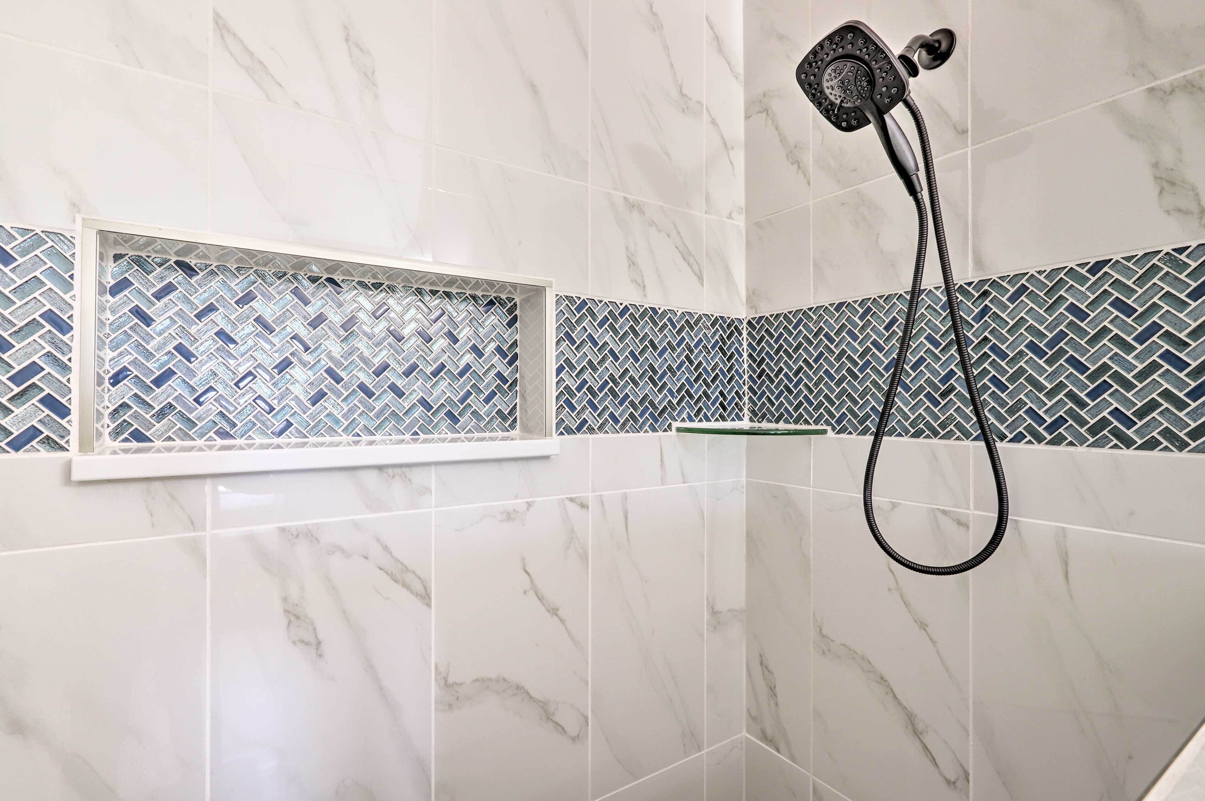 A bathroom with a shower, marble tiles, and a herringbone-patterned tile border.