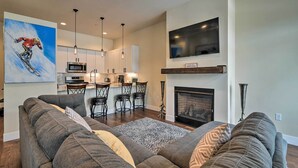 A modern living room with a large sectional sofa, a fireplace, and a kitchen area with a dining table and chairs.