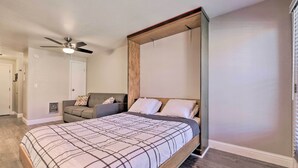 A bedroom with a four-poster bed, a ceiling fan, a gray sofa, and a wooden floor. - Cozy Studio w/ Balcony, Walk to Brian Head Resort! (Brian Head)