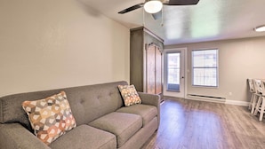 A living room with a gray sofa, patterned pillows, a ceiling fan, and a view of a dining area. - Cozy Studio w/ Balcony, Walk to Brian Head Resort! (Brian Head)