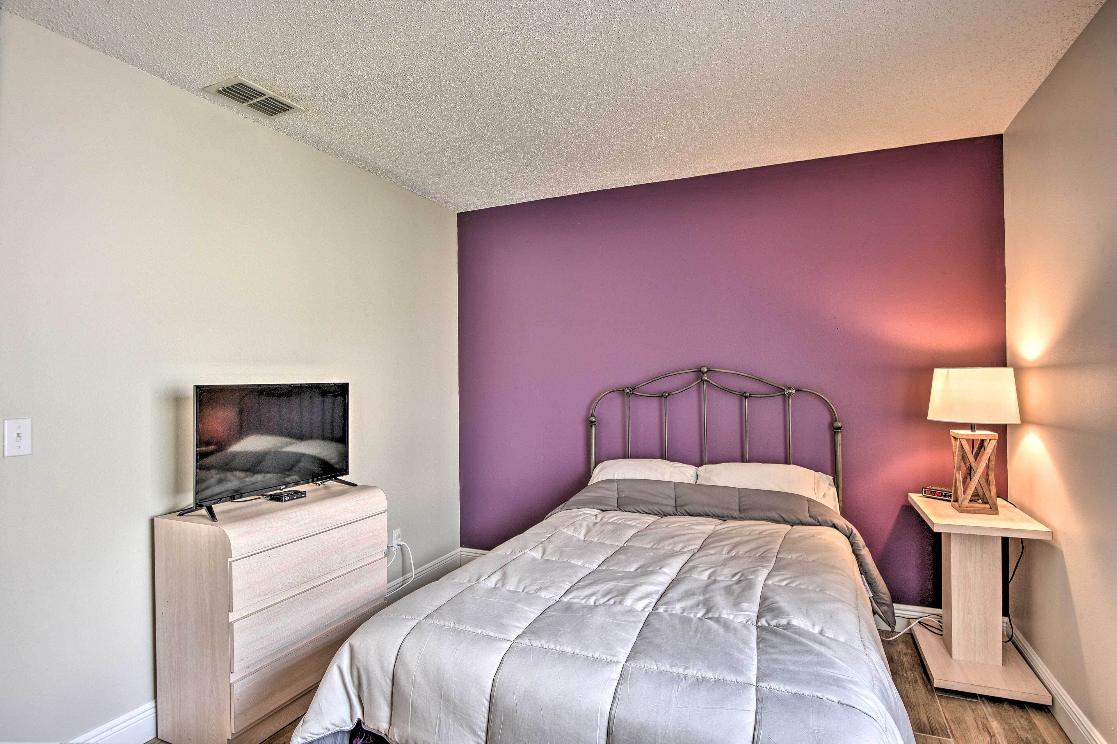 A bedroom with a bed, a dresser, a TV on a stand, and a bedside lamp.