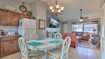 A spacious living area with a dining table, white chairs, a red sofa, and a television.
