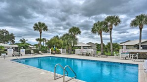 A swimming pool with a 6 ft depth marker, surrounded by lounge chairs and palm trees, under a cloudy sky.