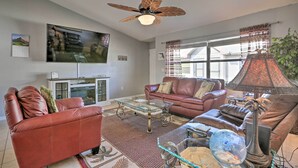 A living room with a ceiling fan, leather sofas, a glass coffee table, a TV, and a lamp.