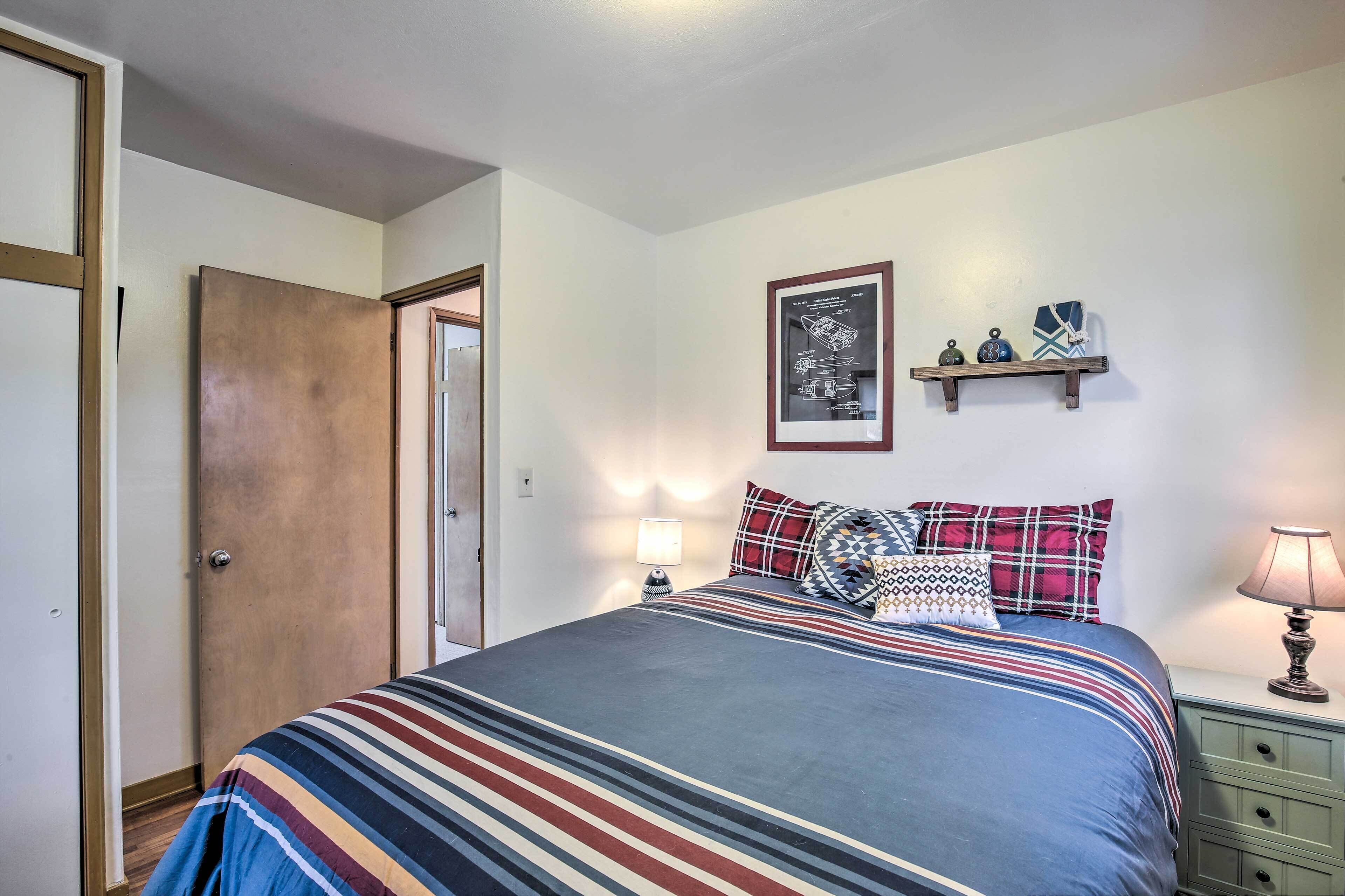 Un dormitorio con cama, mesita de noche, estante en la pared y una puerta.