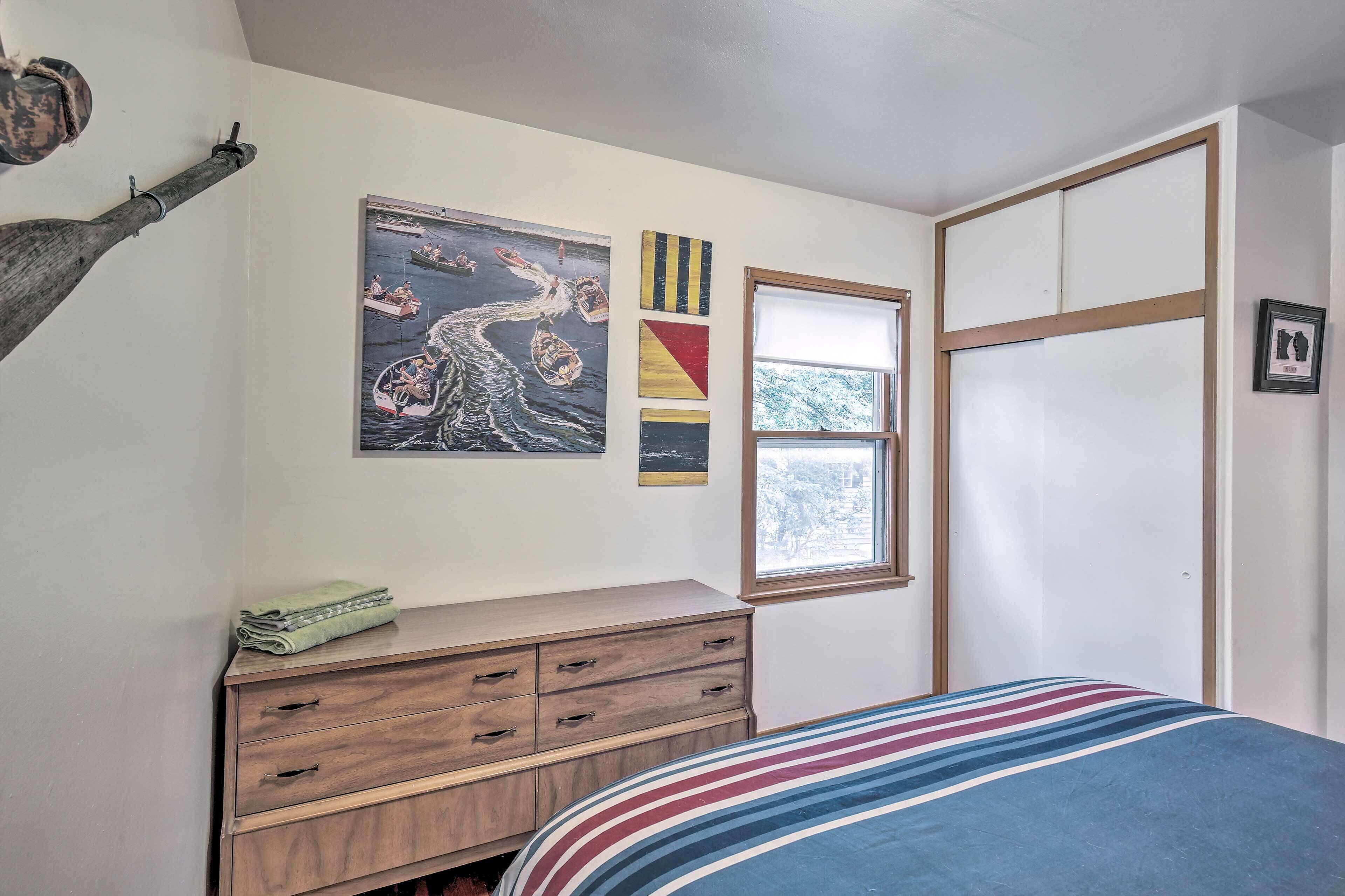 Un dormitorio con cama, cómoda de madera, ventana y obras de arte en la pared.