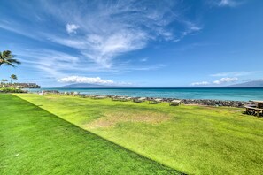 A grassy area with lounge chairs and a view of the ocean. - Beachfront Condo: Sunset Views & Pool Access! (Napili-Honokowai)