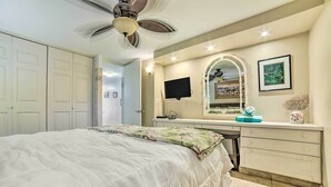 Una camera da letto con un letto, una toeletta con specchio, una ventola a soffitto e una porta che dà su un'altra stanza.