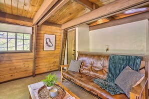 A cozy room with a leather sofa, wooden walls, a window with blinds, and a framed picture on the wall. - Pet-friendly Cottage, Walk From Big Bear Village! (Big Bear Lake)