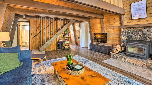 A cozy cabin interior with a wooden staircase, a fireplace, and a living area with a sofa and a coffee table. - Pet-friendly Cottage, Walk From Big Bear Village! (Big Bear Lake)