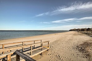 Un muelle de madera que conduce a una playa arenosa, con huellas, un cielo despejado y un mar tranquilo.