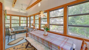 A cozy room with large windows, a sofa, a dining table, and a ceiling fan. - Walk to Beach: Long Island Wine Country Home! (Cutchogue)