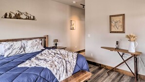 A bedroom with a bed, bedside tables, a wooden bench, a wall-mounted shelf, and a small table with a vase. - Cozy Columbia Falls Condo w/ Private Balcony! (Columbia Falls)