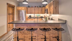 A kitchen with wooden cabinets, a stainless steel refrigerator, a central island with stools, and pendant lighting. - Cozy Columbia Falls Condo w/ Private Balcony! (Columbia Falls)