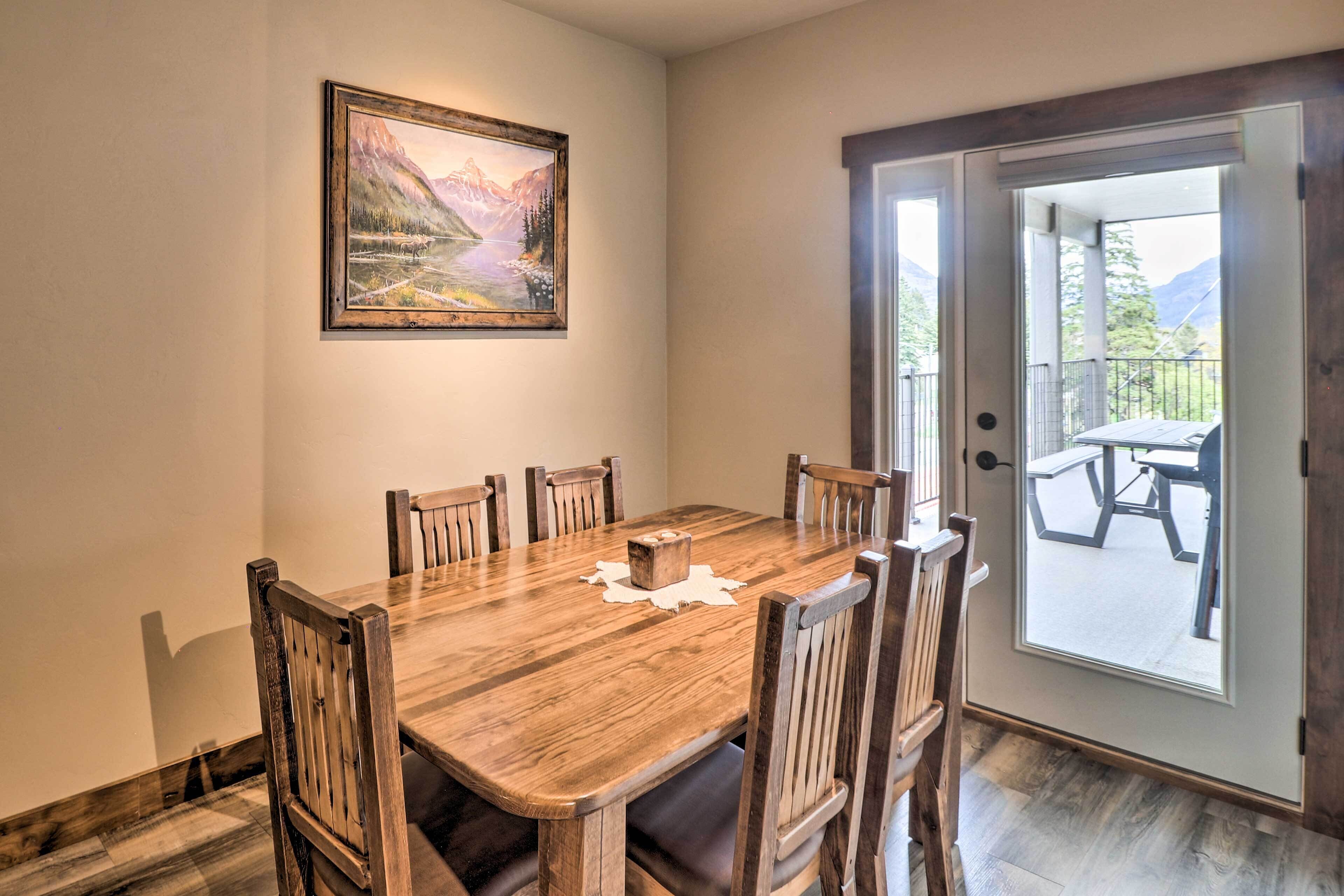 A dining area with a wooden table and chairs, a painting on the wall, and a door leading to an outdoor patio.
