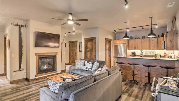 A modern living room with a fireplace, a sofa, and a kitchen area with bar stools. - Cozy Columbia Falls Condo w/ Private Balcony! (Columbia Falls)